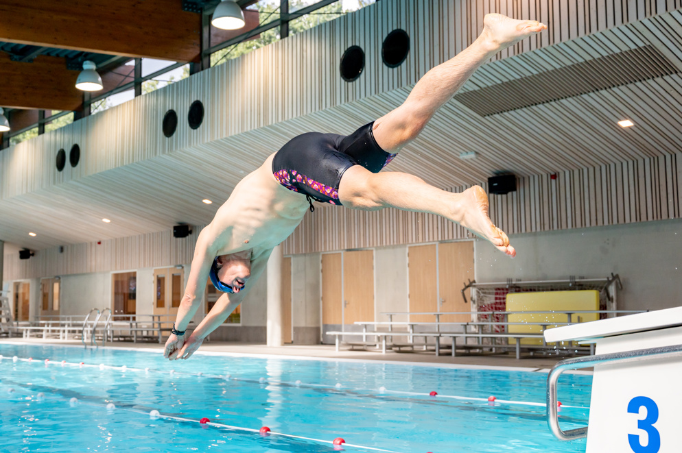 Een zwemmer duikt het water in vanaf startblok drie