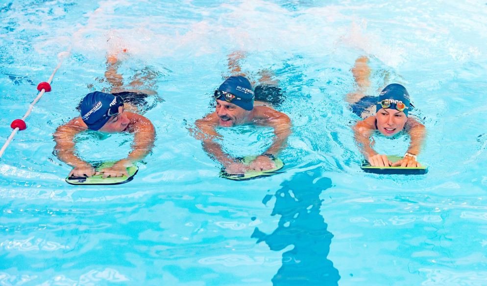 Drie zwemmers zwemmen benen met een zwemplankje